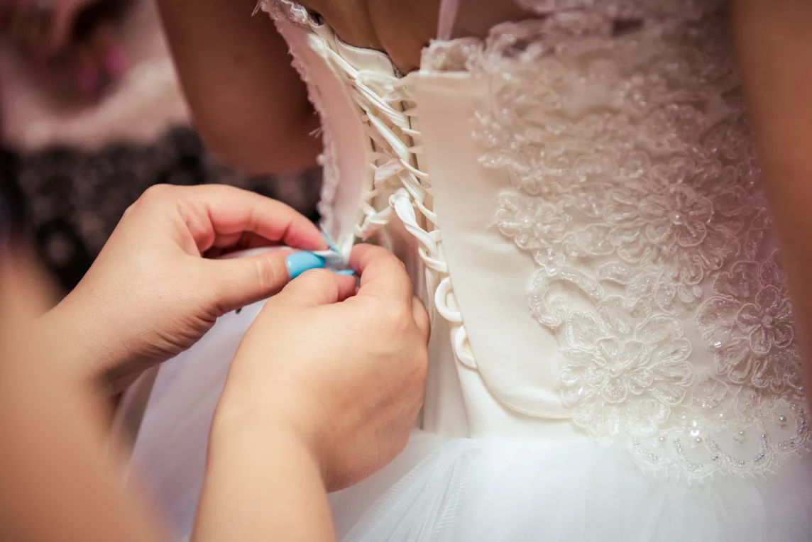 A person tying a corset on the back of a wedding dress.