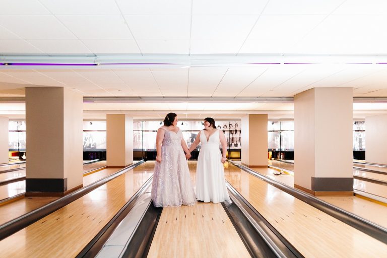 Two brides stand on a bowling alley lane holding hands at Pinstripes DC