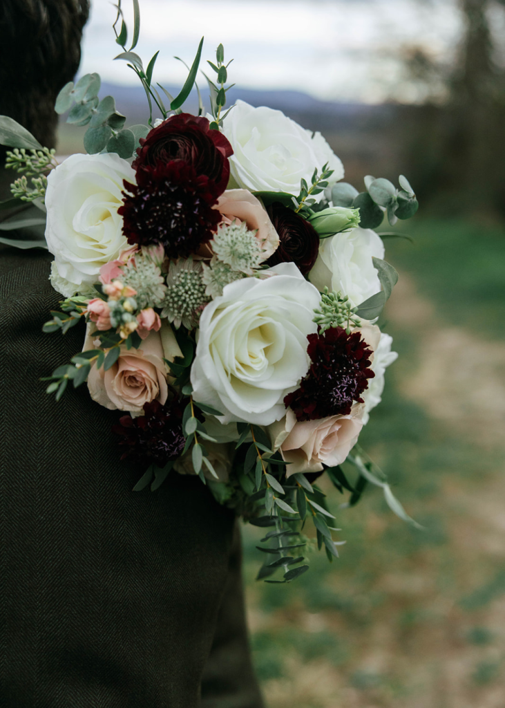 a newlywed carries a bouquet with dark red, white, and pink roses and greenery