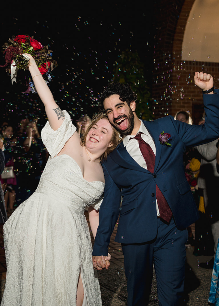 newlyweds smile at the camera as guests blow bubbles