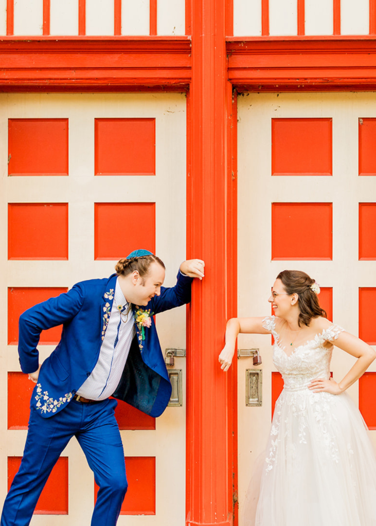 Two spouses smile at one another in front of a red door at Glen Echo park