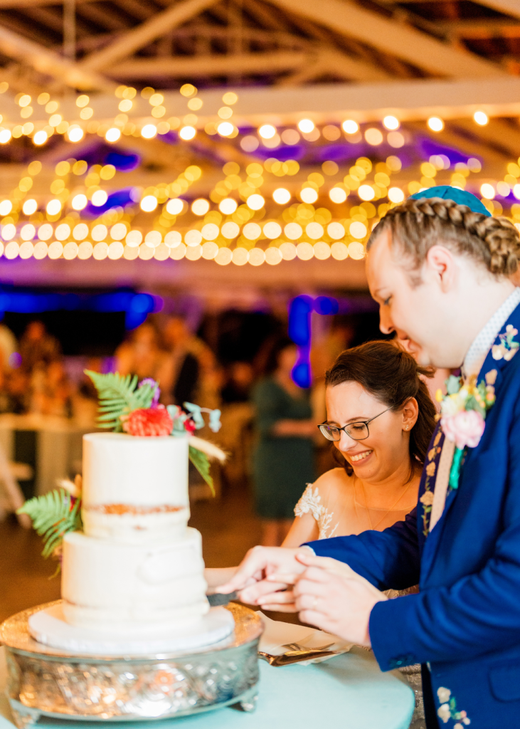 two spouses cut the wedding cake under string lights at glen echo park