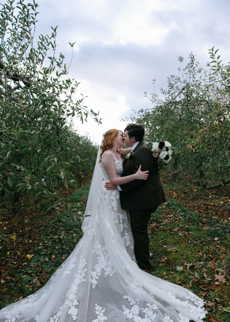 newlyweds embrace with a kiss in the middle of an orchard
