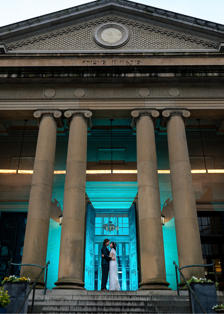 newlyweds stand in front of the entrance to the line hotel between the columns