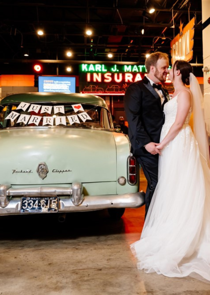 bride and groom inside the Baltimore Museum of Industry next to a car that says Just Married