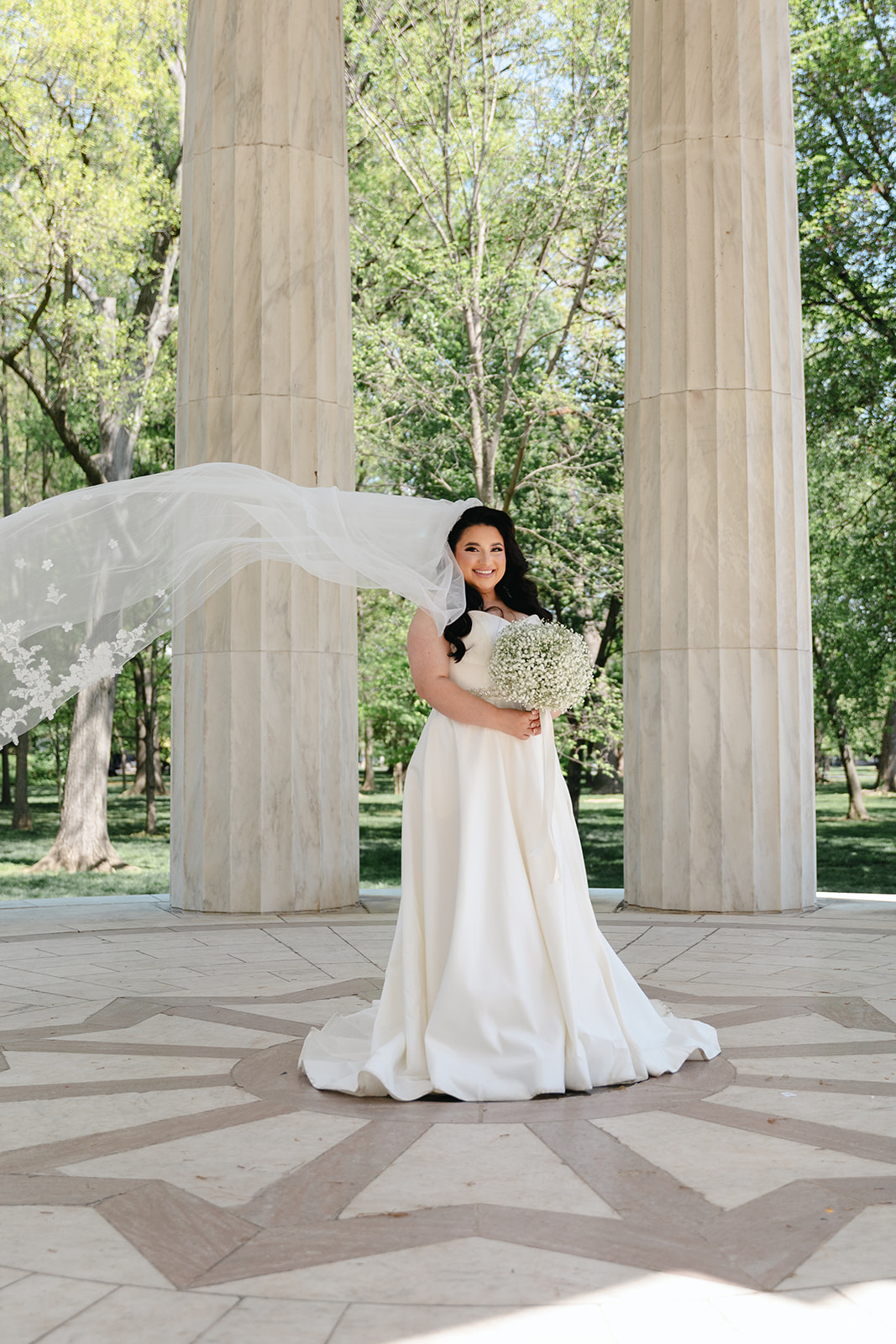 Washington, DC War Memorial wedding portrait of bride standing holding bouquet and her veil flowing behind her with the wind