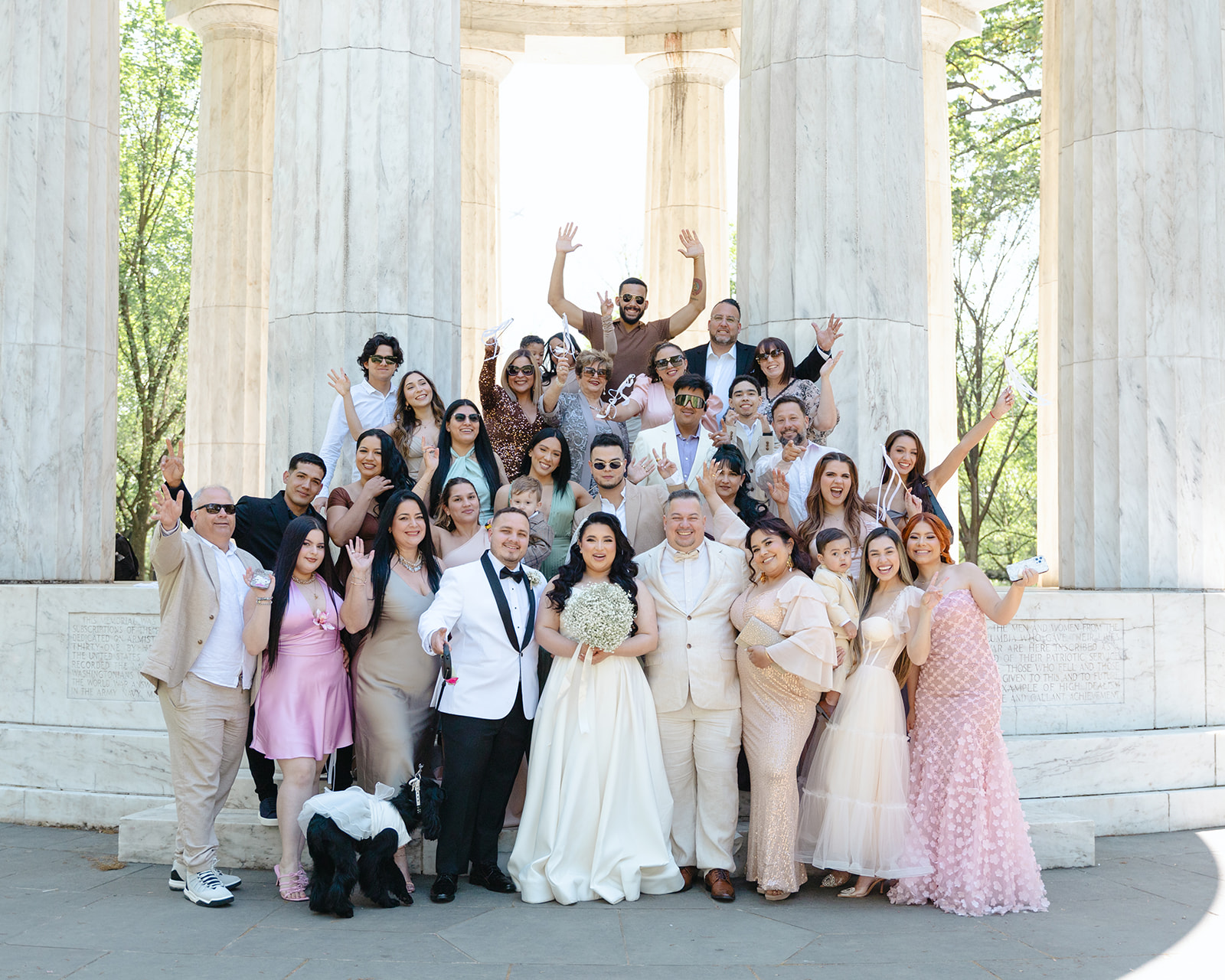 Portrait of the wedding couples family posting excitedly with hands up and smiling in front of the Washington, DC War Memorial
