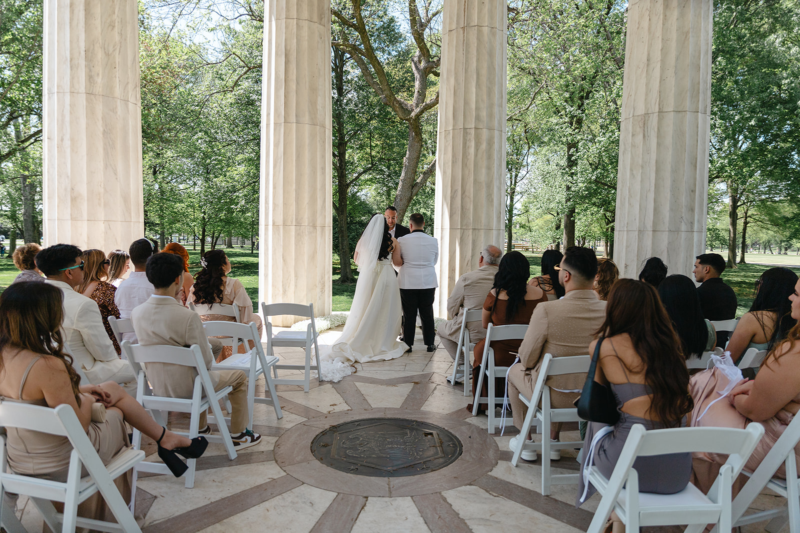 Washington, DC War Memorial wedding ceremony with the bride and groom at the end of the aisle, and guests to the side, watching in their chairs as they exchange vows