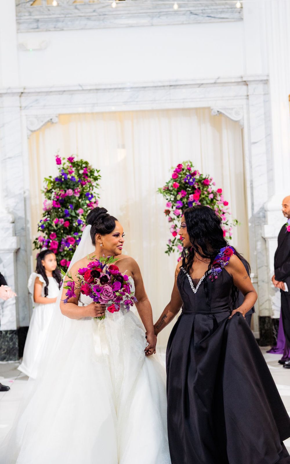 Two brides, one in a black dress and one in a white dress, hold hands at Citizens Ballroom in Frederik, MD