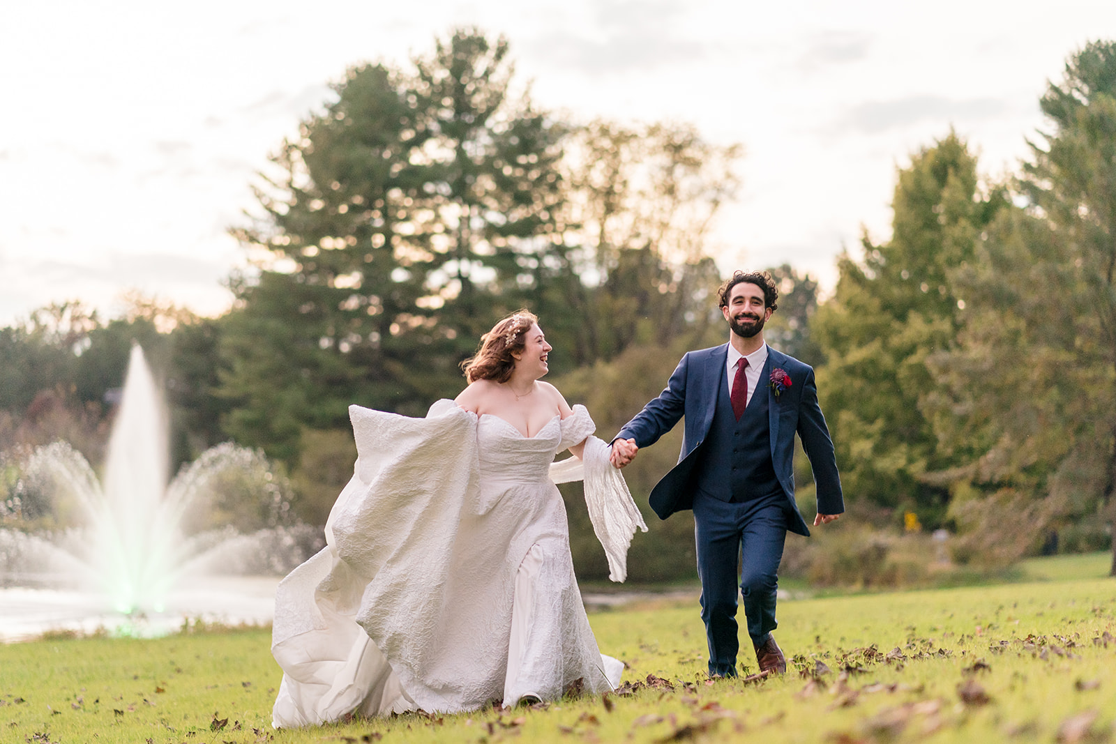 couple holding hands and running through field with sprinkler on in background