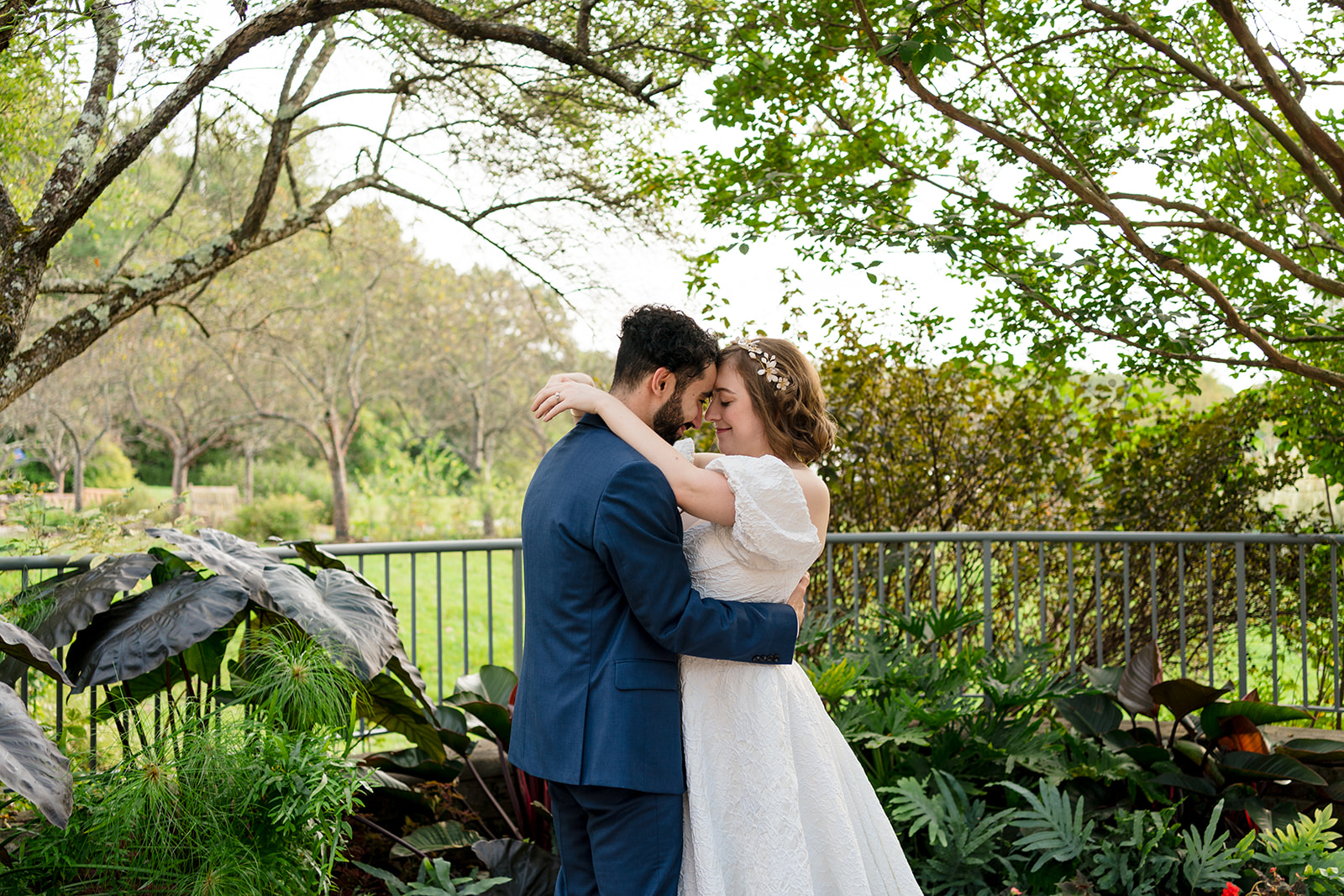 Couple holding each other in garden greenery with foreheads at one another