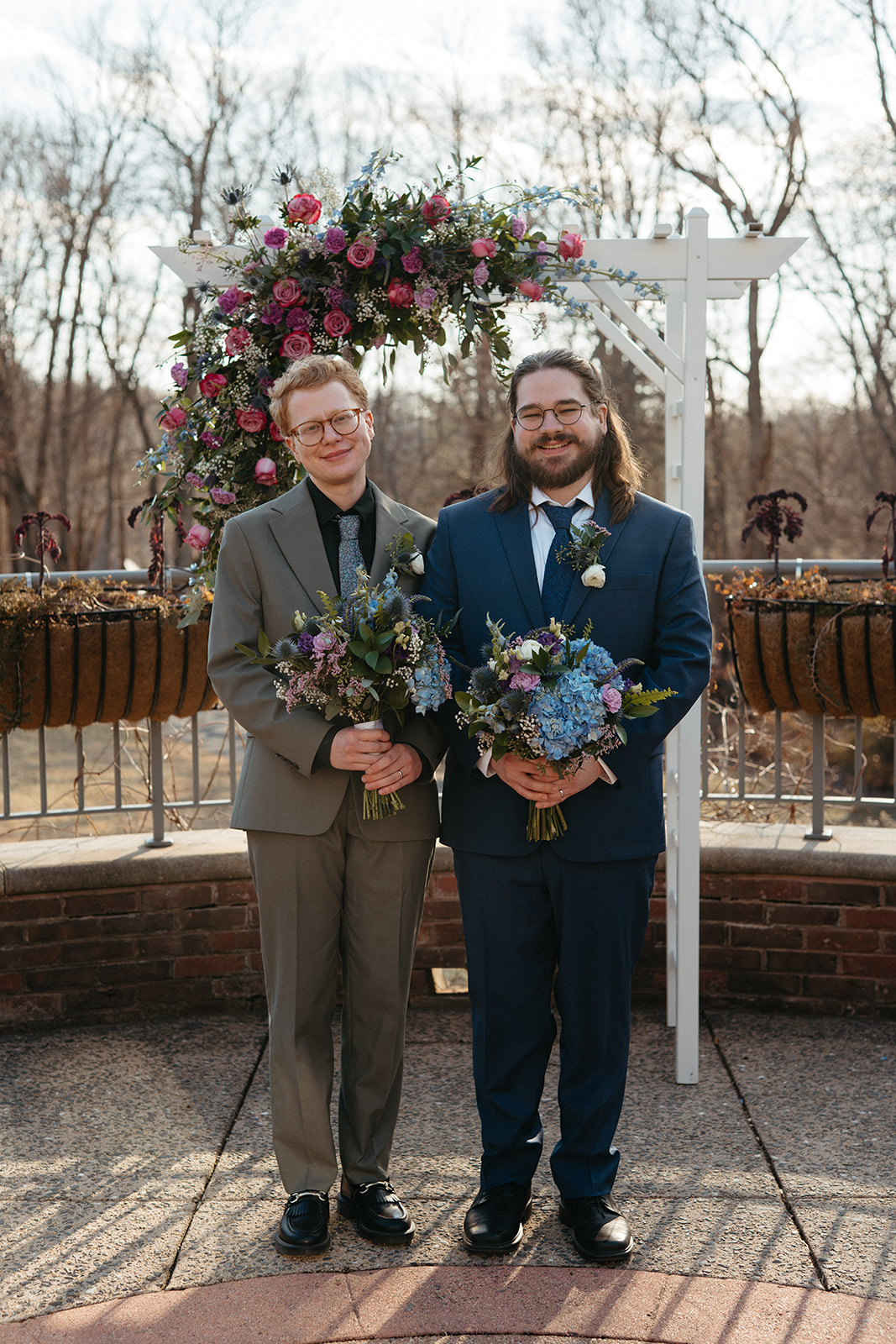 couple holding vibrant bouquets under their wedding arch