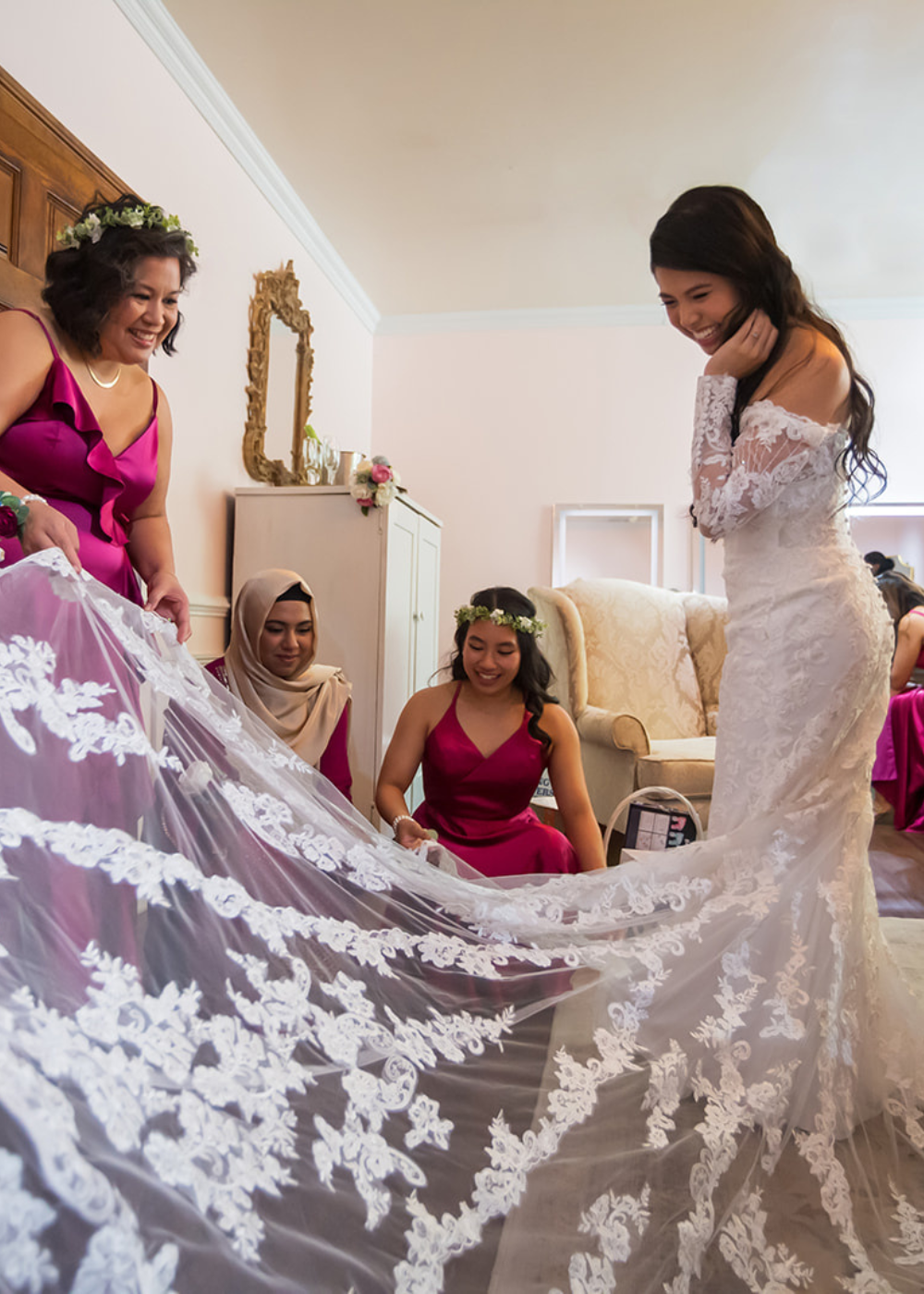 wedding party members in pink dresses admire the detail of the bride's wedding dress while the bride smiles inside the getting ready suite at Running Hare Vineyard