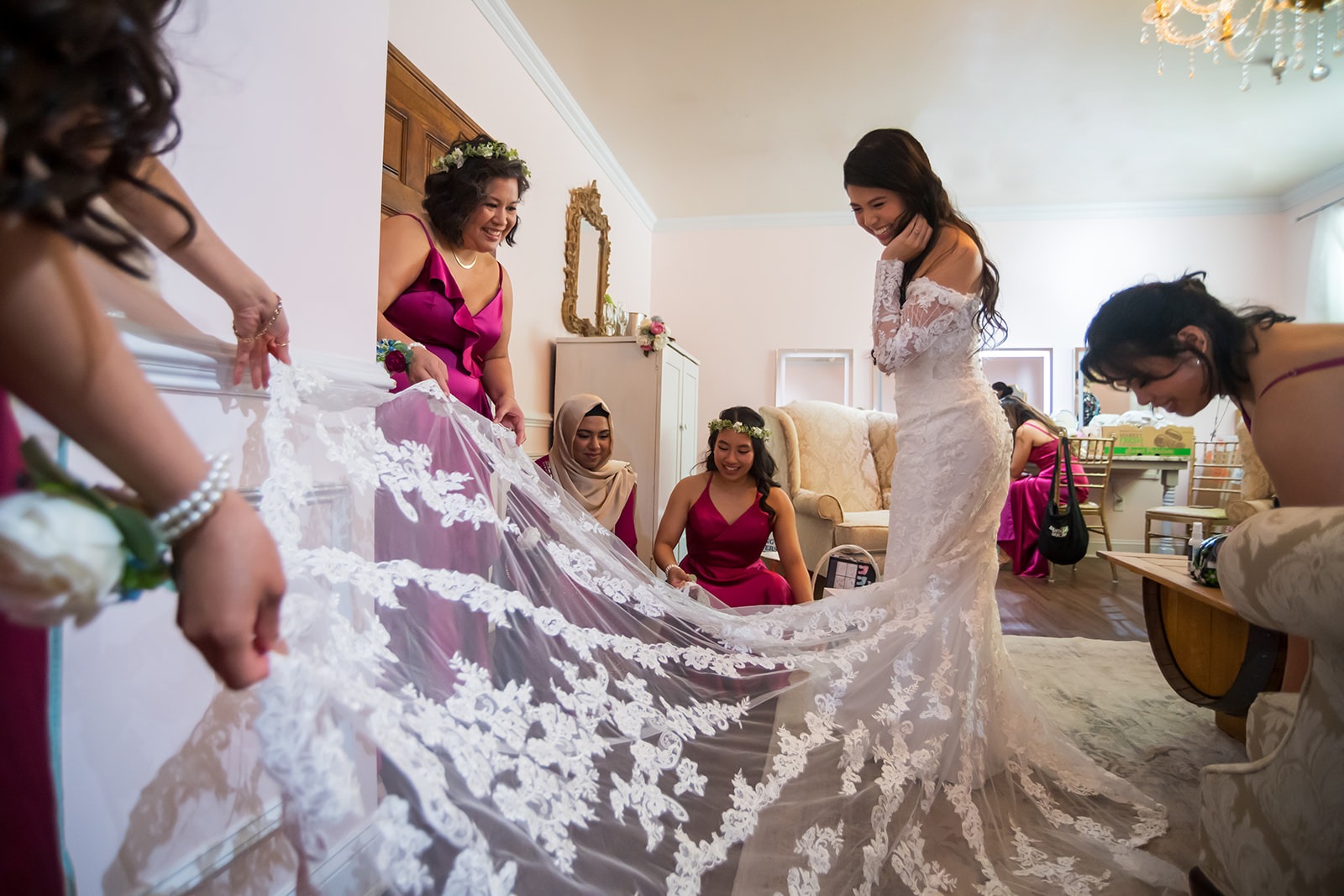 bridesmaids fluffing out the train to bride's dress as they all laugh