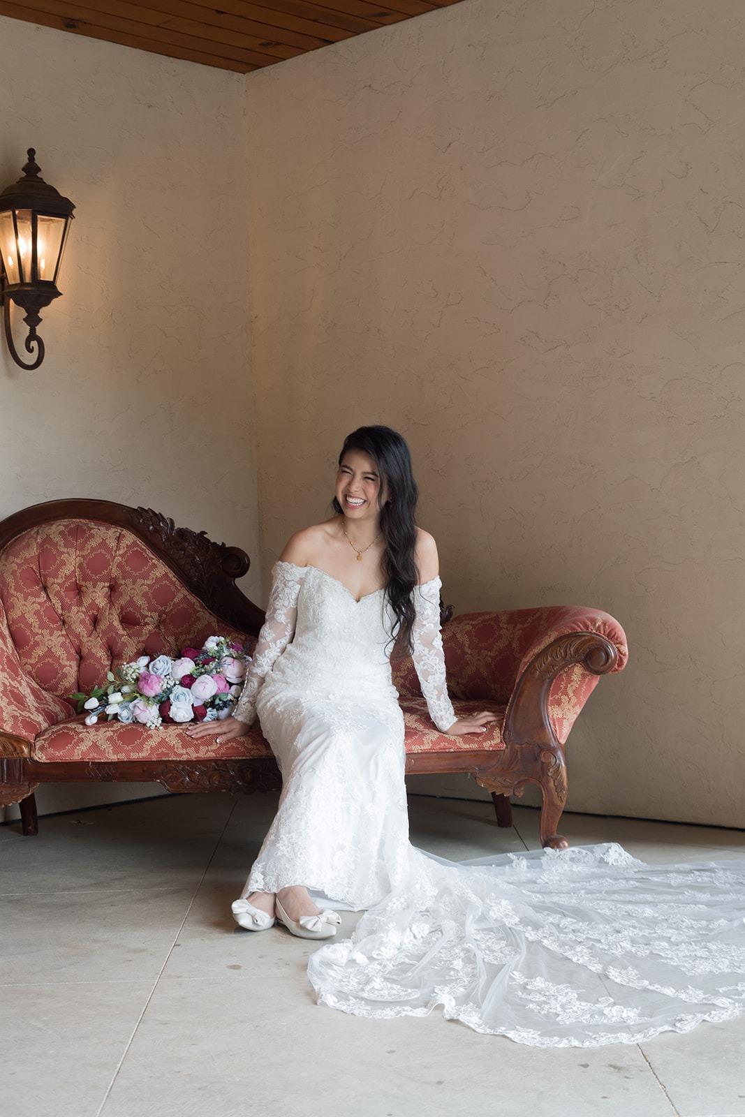 wife sitting on couch laughing with dress spread out and bouquet by her side