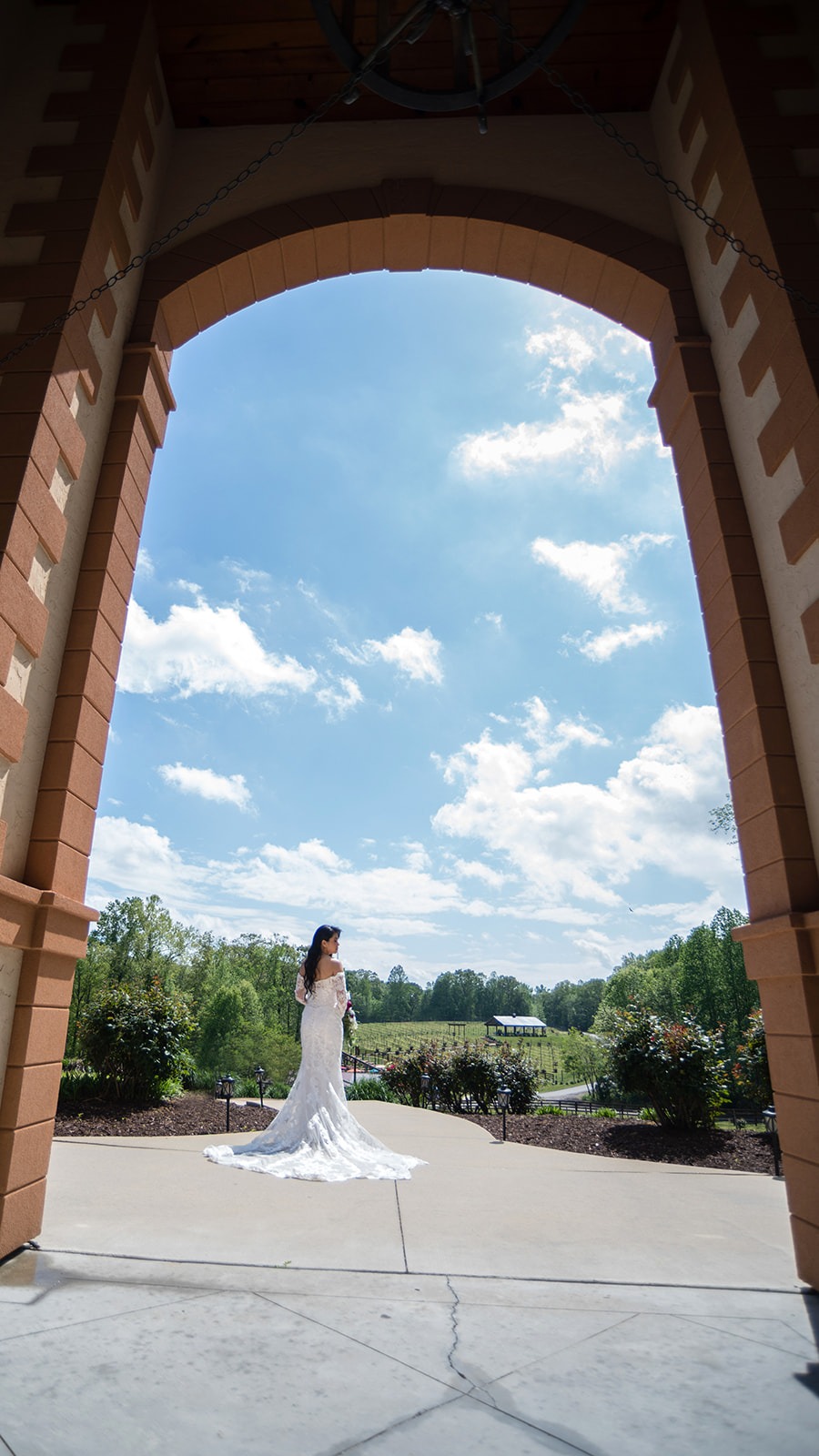 wide shot of bride looking back into stone archway showing the vineyard landscape in front of her