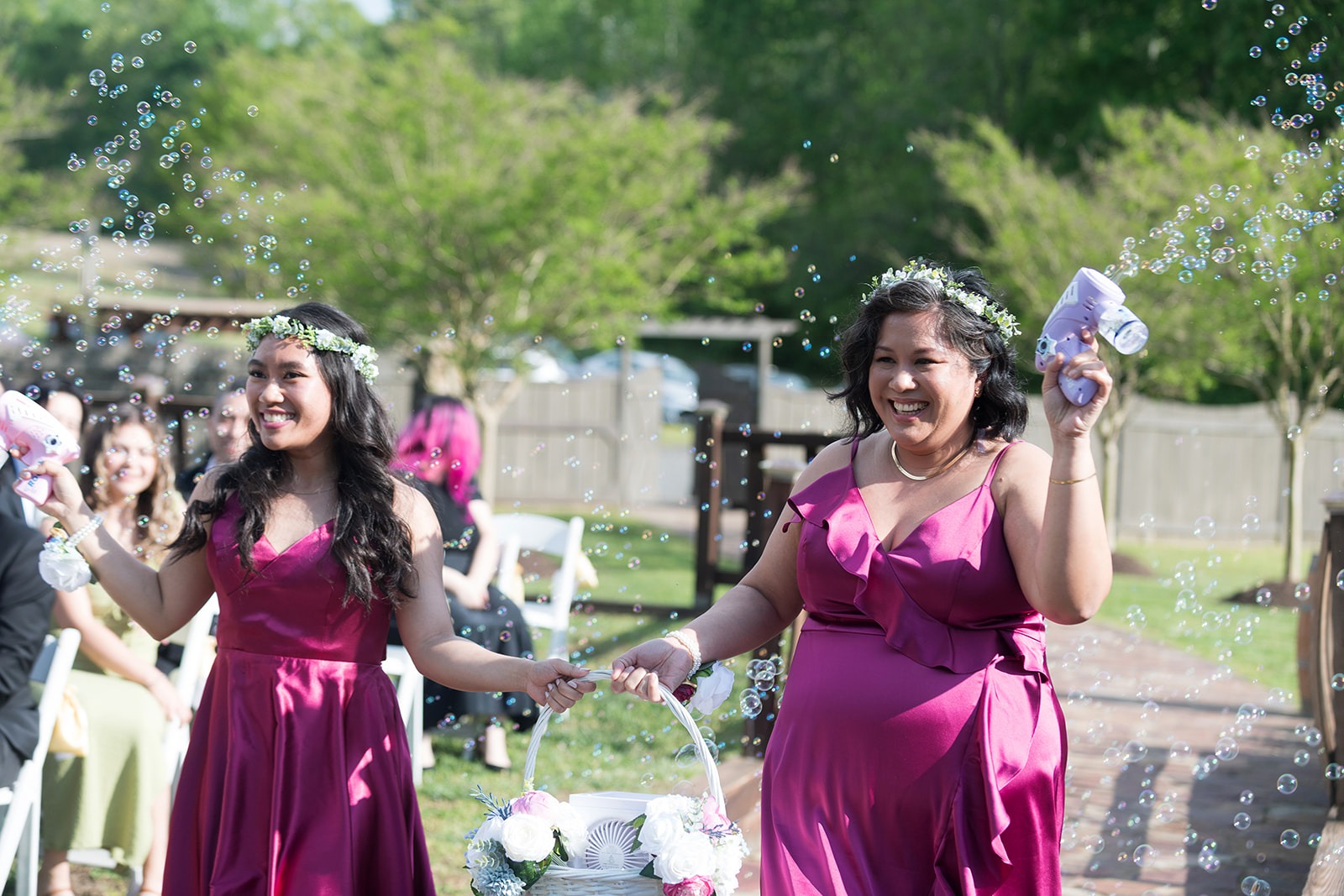 bridesmaids walking down ailse in magenta dresses with flower crowns and bubble guns