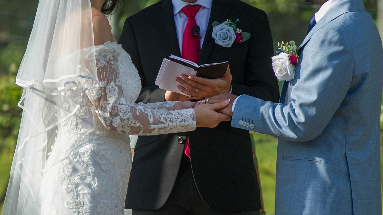 close up of bride and groom holding hands at the alter with officiant in between reading