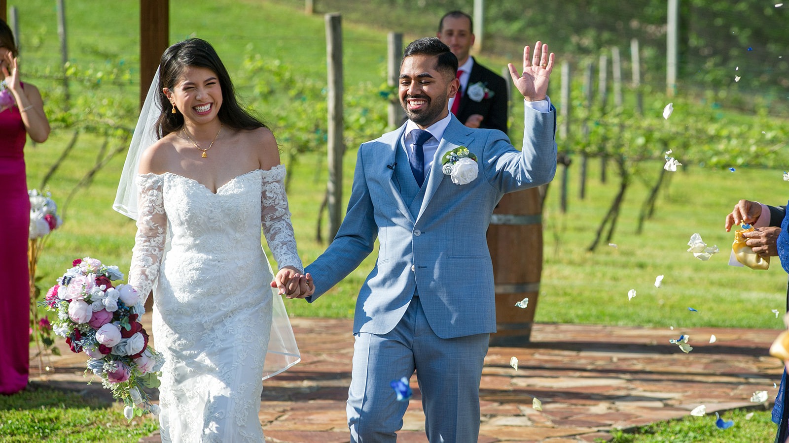 couple holding hands and waving in the aisle celebrating with petals being tossed
