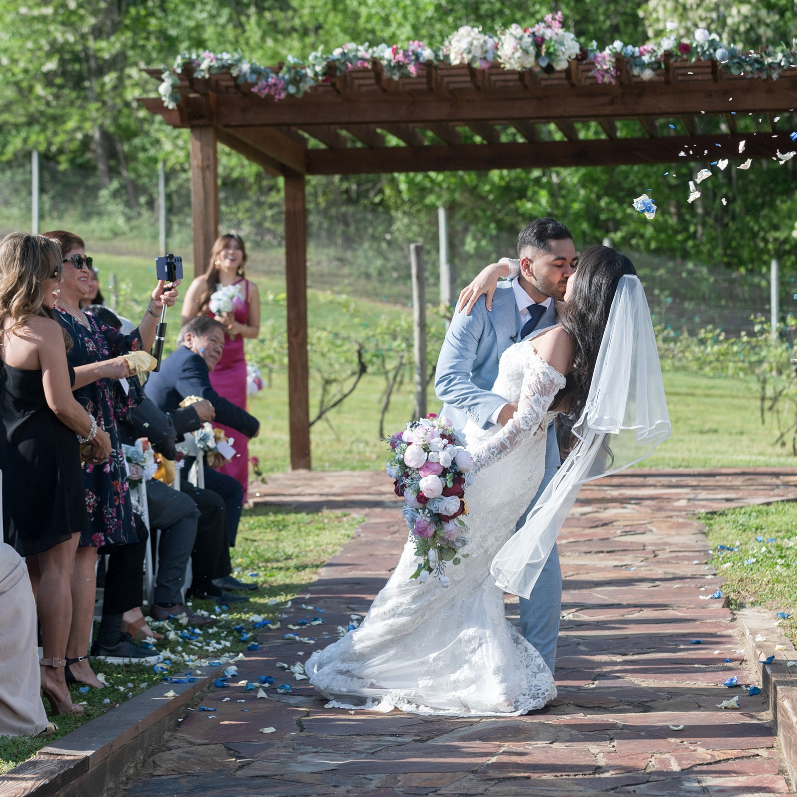 groom and bride kissing in the aisle with petals being tossed above them