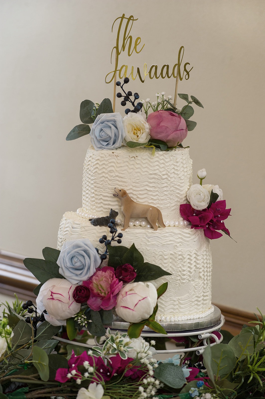 Close up of the white cake decoarted with pink, blue, and white flowers along with a detail of their dogs on the cake and their last name on top